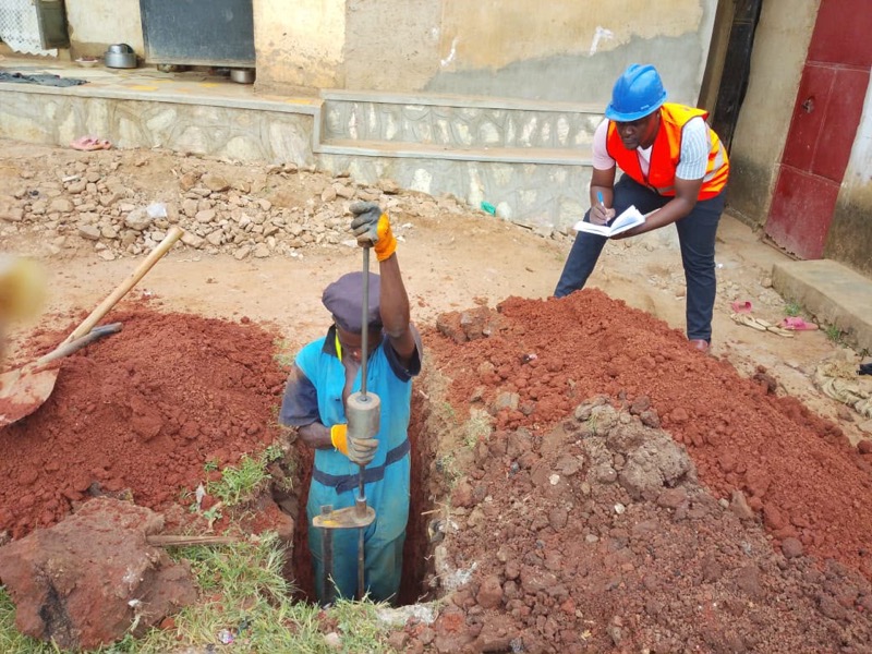 A BANEC engineer in a hard hat and hi-viz vest recording readings during an on-site geotechnical soil survey.